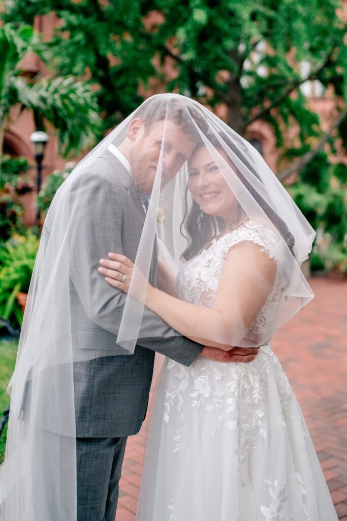A bride and groom with the veil draped over them for a romantic portrait after their Immaculate Conception Church wedding