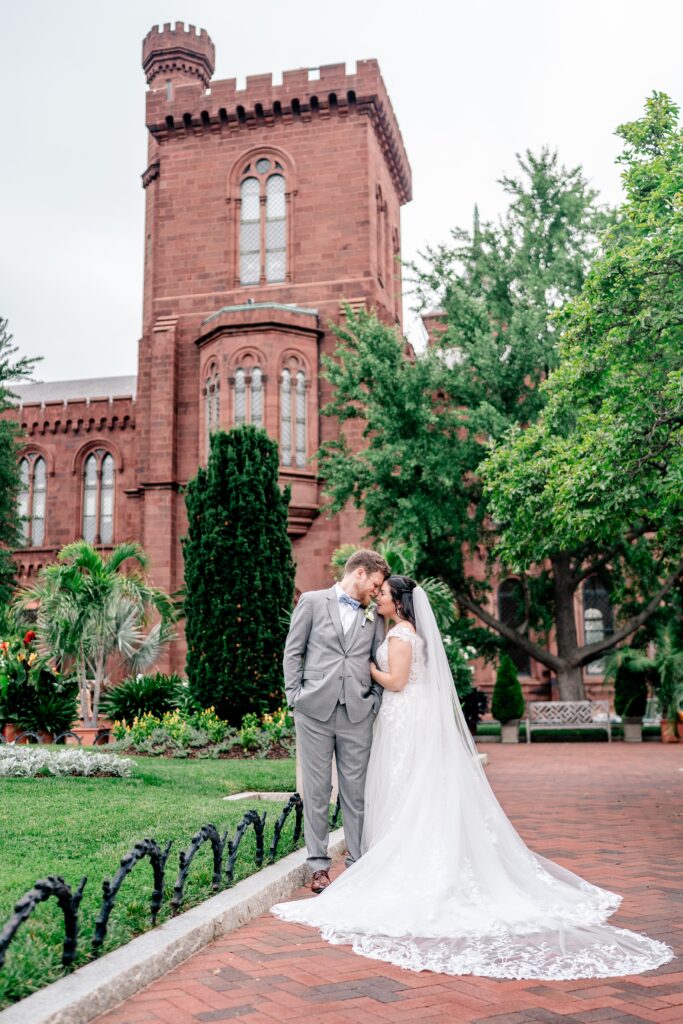 A bride and groom sharing a sweet moment together in front of the Smithsonian Castle in the Enid A. Haupt Gardens