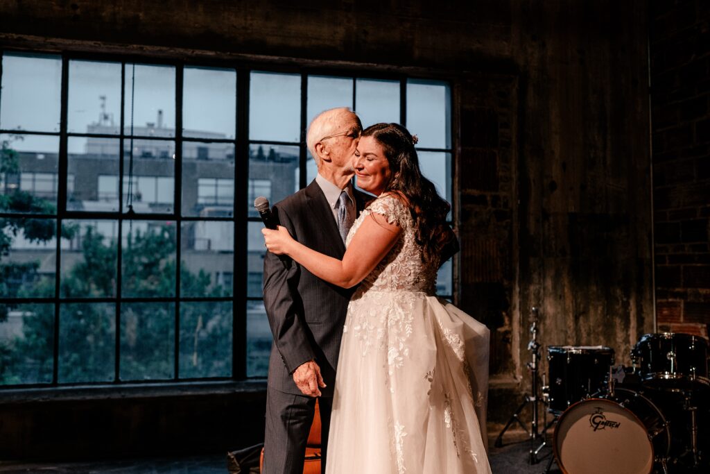 A bride's dad kissing her cheek after they sang a duet together in a photo by a Washington DC wedding photographer