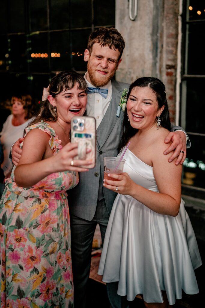A bride and groom taking a selfie with one of their wedding guests at their reception