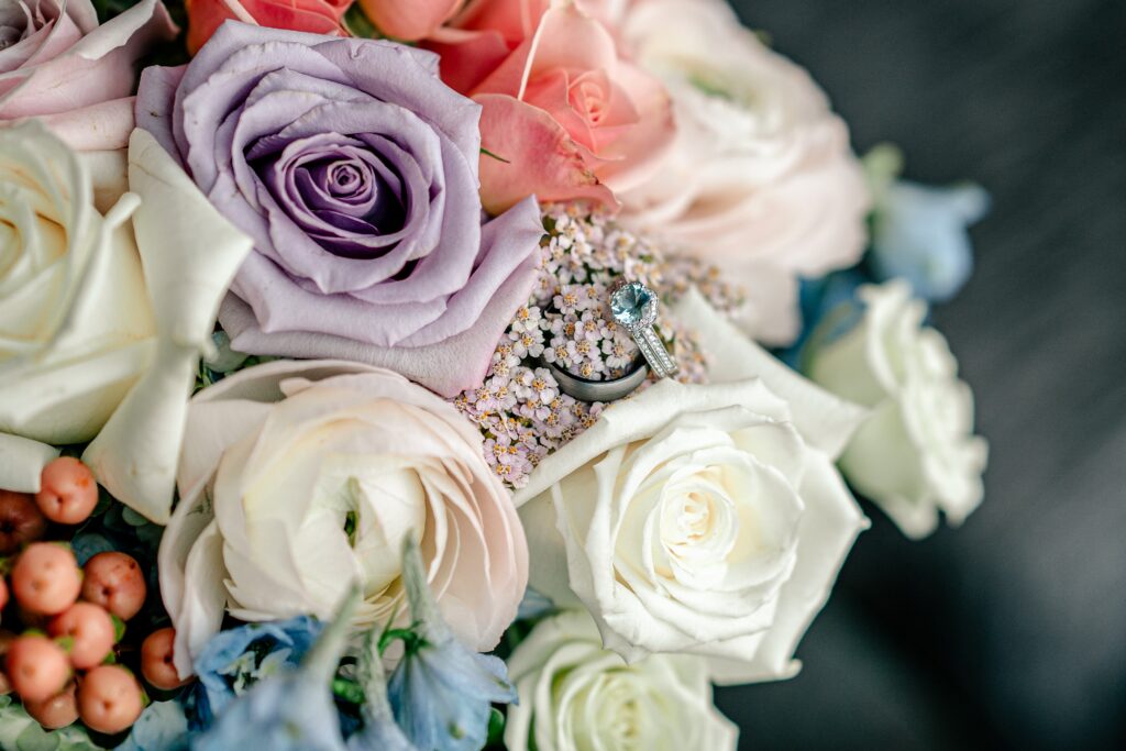 A wedding ring set featuring a blue stone engagement ring sitting in a bridal bouquet by a Northern Virginia wedding photographer