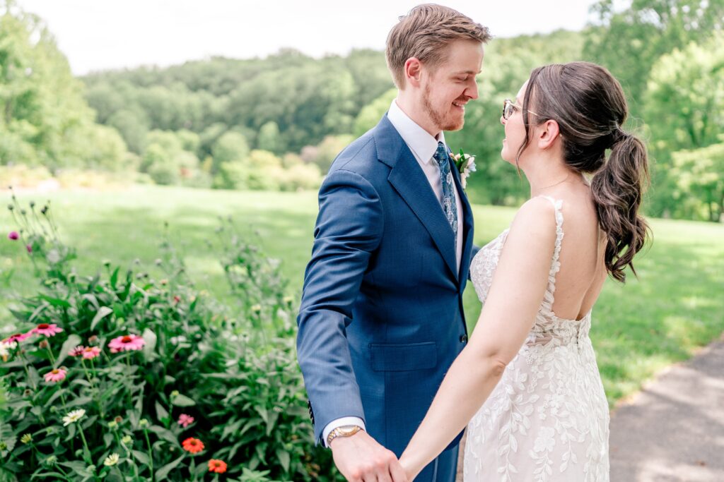 A bride and groom smile at each other in a garden