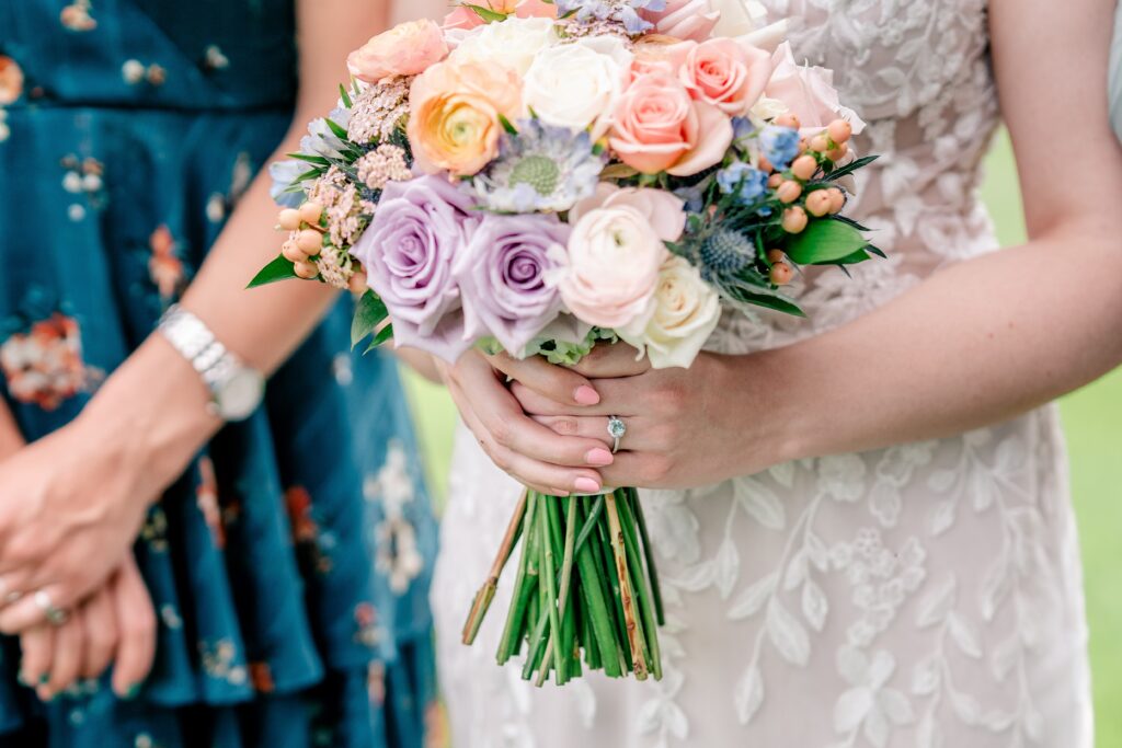 A close up of a bride's hands holding her colorful bouquet and her engagement ring with a blue stone in focus
