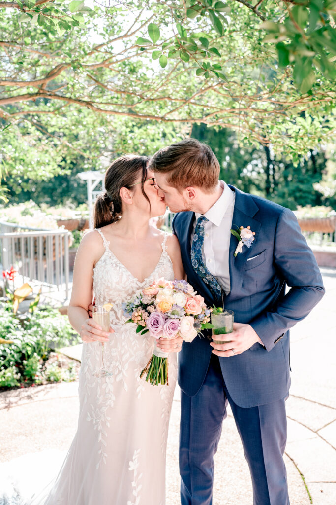 A bride and groom share a kiss while holding cocktails