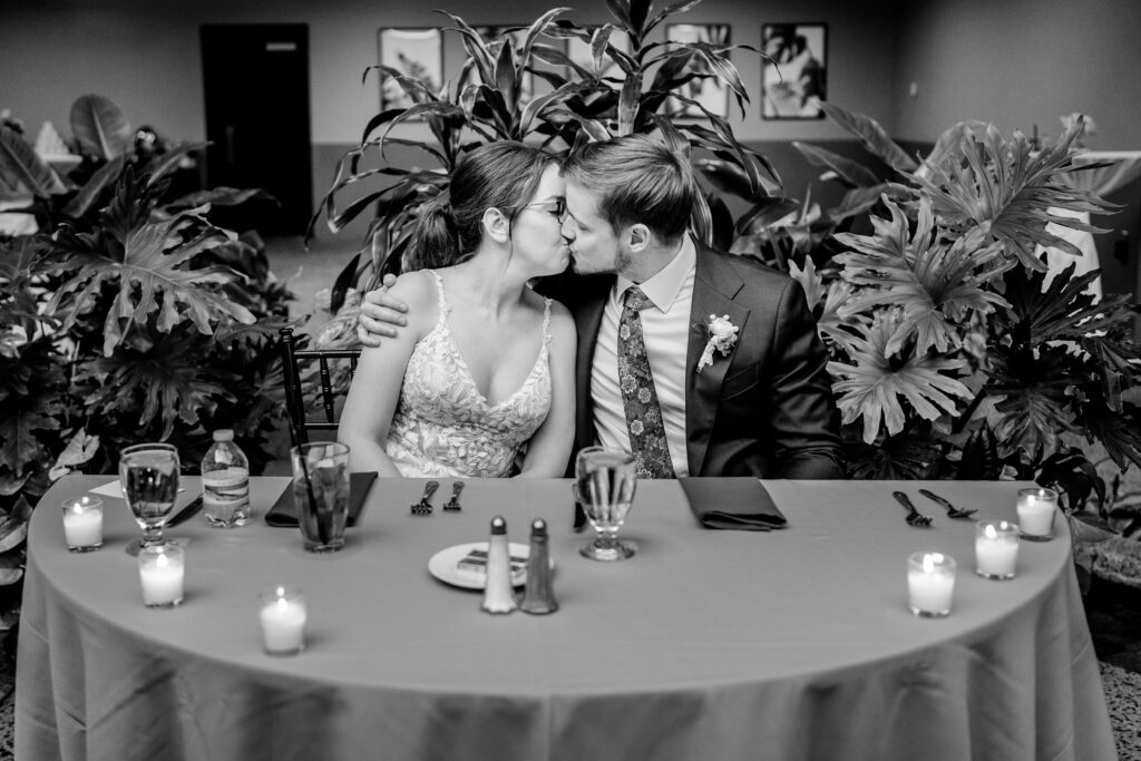 A bride and groom share a kiss at their sweetheart table during an Atrium at Meadowlark wedding