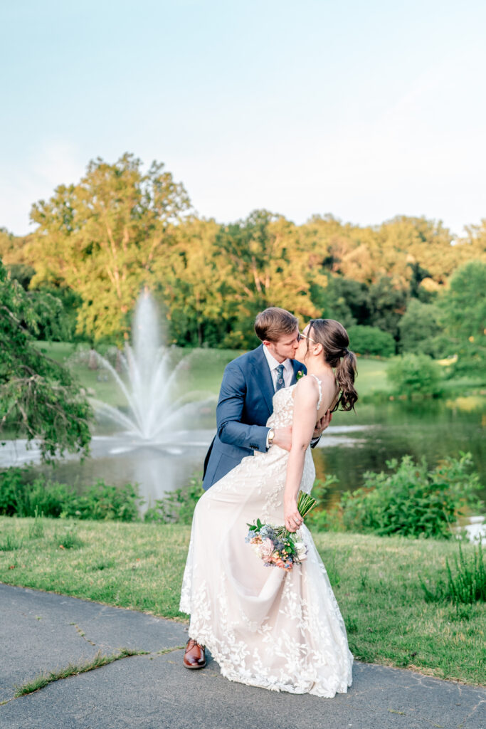 A bride and groom share a romantic mini dip kiss in front of a fountain at golden hour