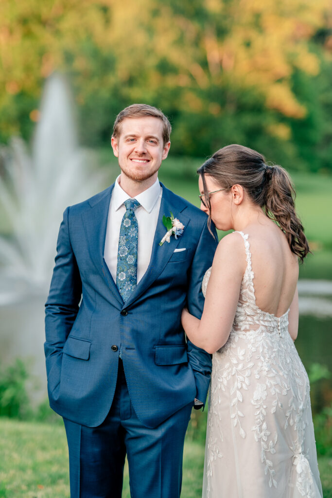 A bride kisses her groom's shoulder as he smiles at the camera during their Meadowlark Botanical Gardens wedding
