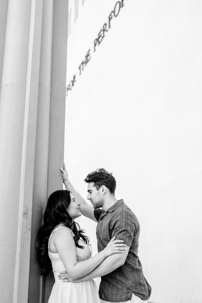 An engaged couple posed against a column wrapped in each other's arms and looking at each other