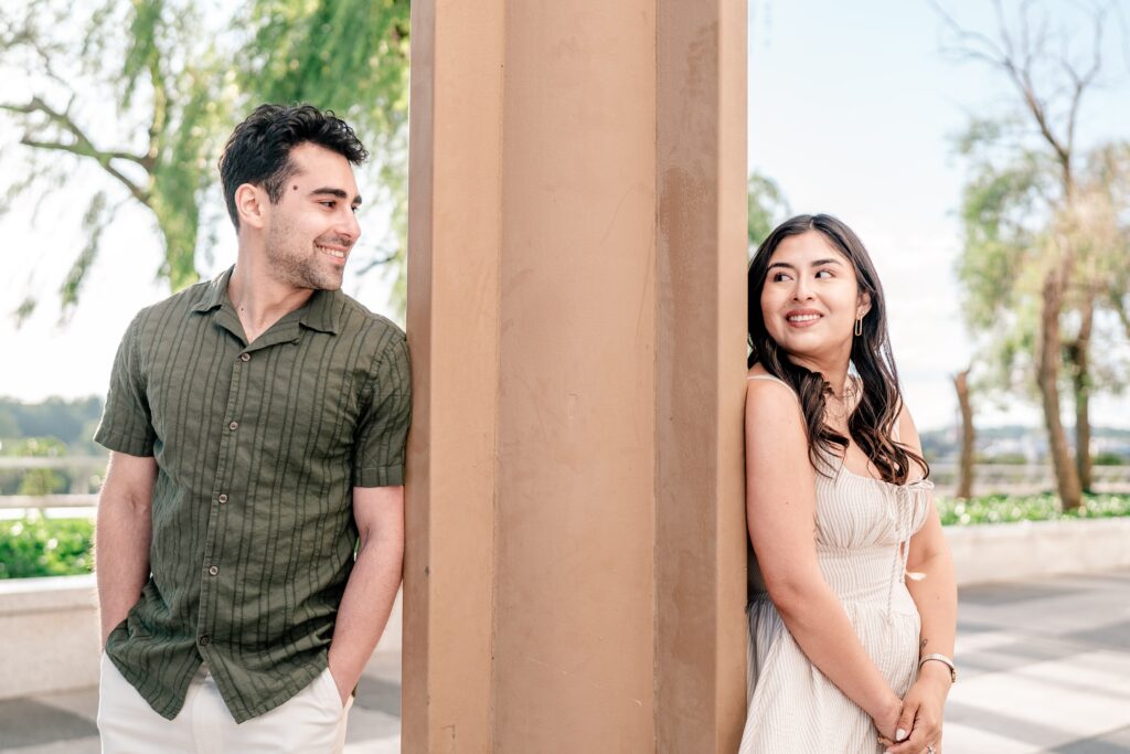 A couple looking at each other around a column during their Kennedy Center engagement photos
