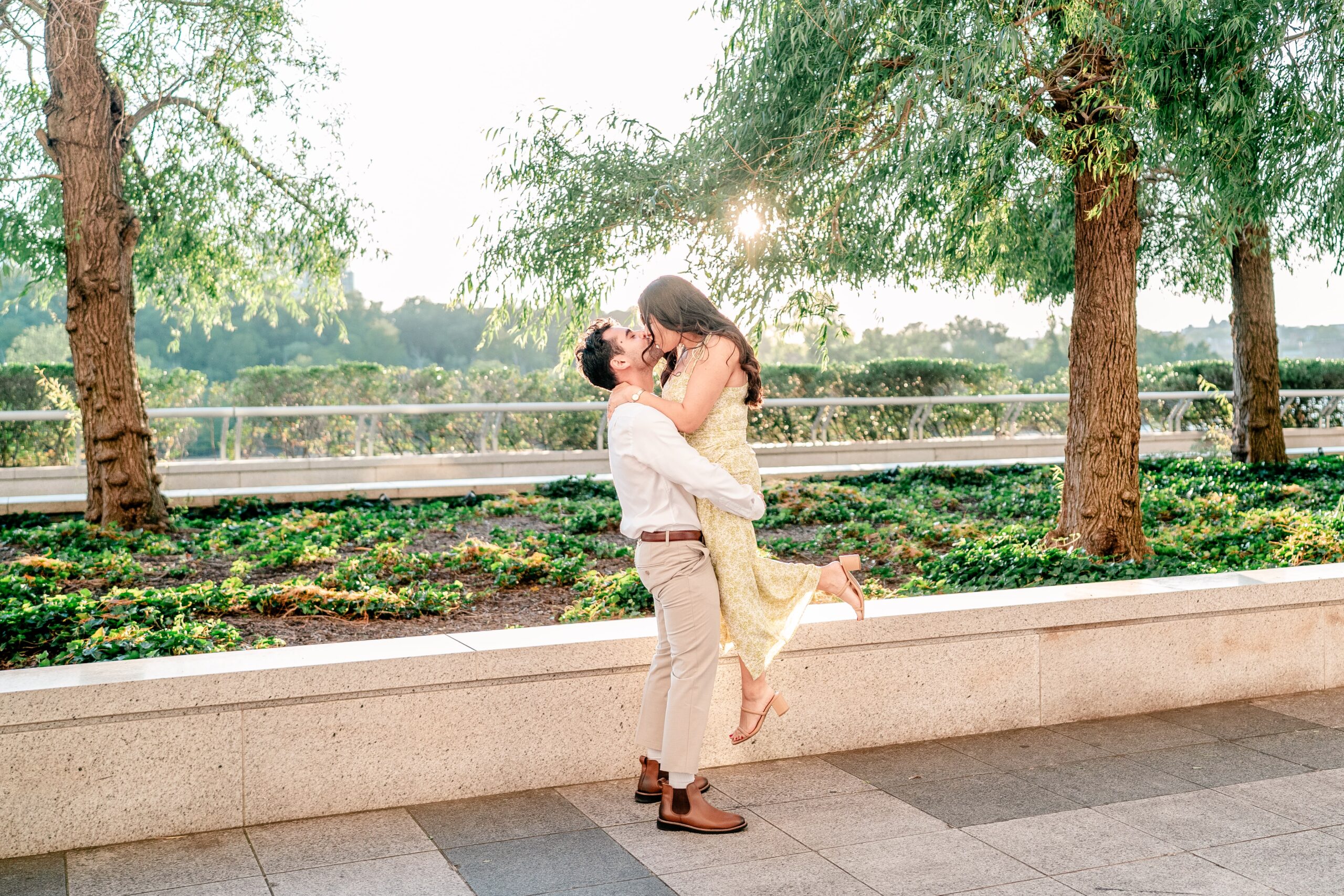 A couple sharing a kiss as he lifts her off her feet on the terrace at golden hour during their Kennedy Center engagement photos