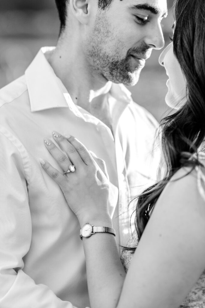 A black and white image of a woman's hand resting on her partner's chest with her large engagement ring shining during their Kennedy Center engagement photos