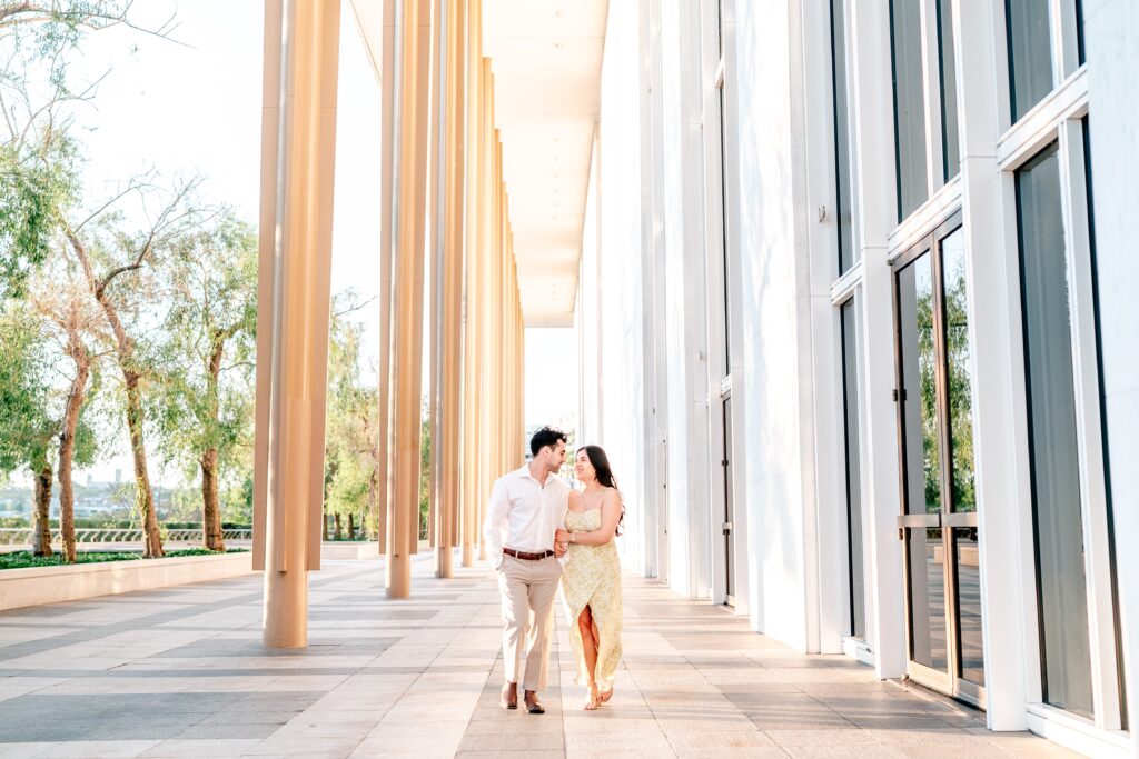 An engaged couple walking together along a terrace between columns at golden hour