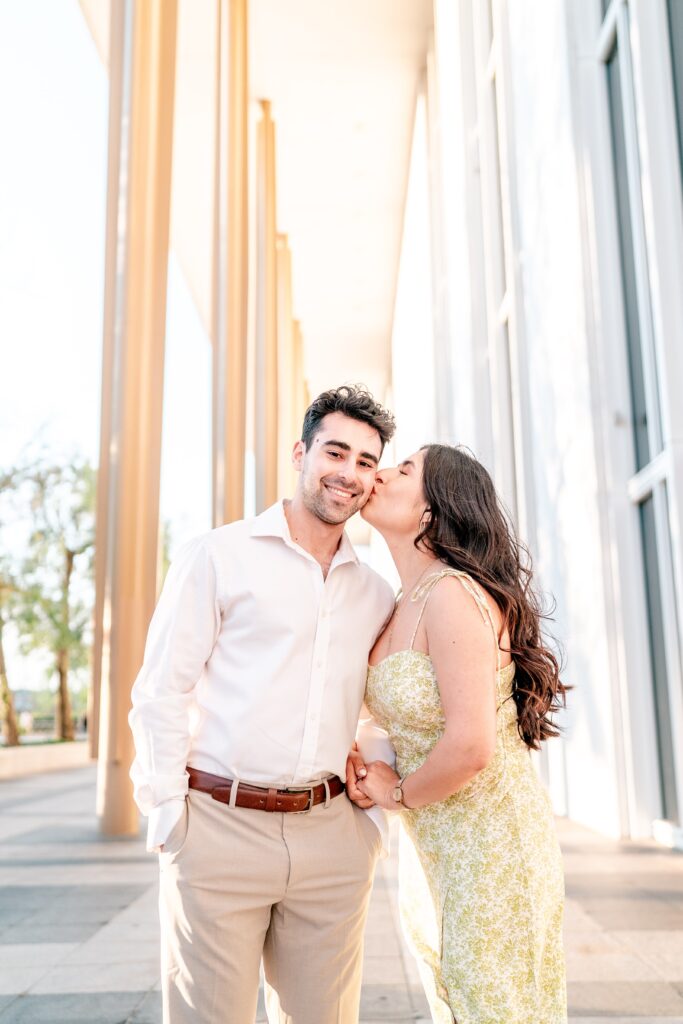 A woman kissing her partner on the cheek as he smiles at the camera at one of the best places to take engagement photos in DC