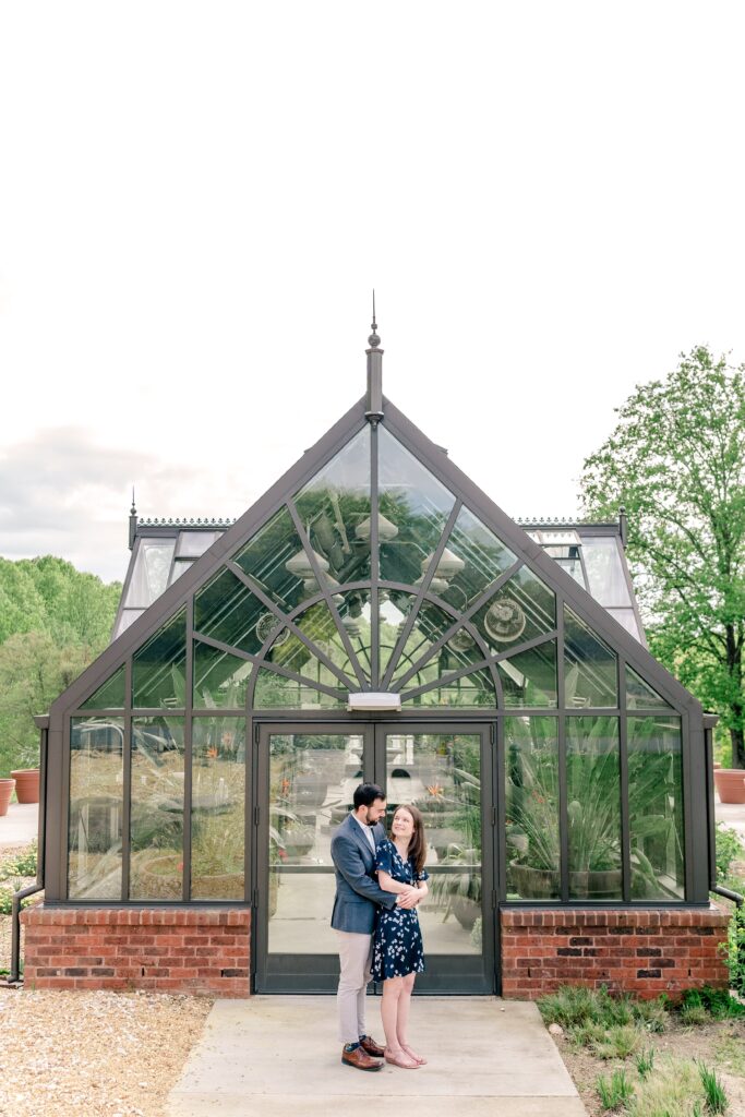 An engaged couple poses in front of a greenhouse