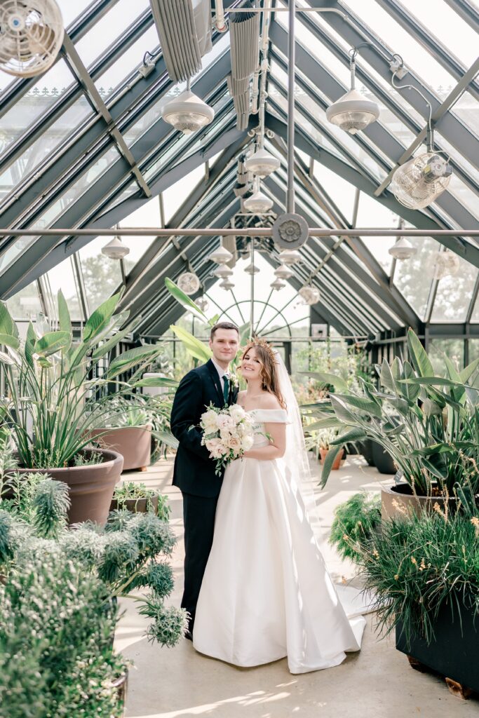 A couple smiling at the camera from inside a greenhouse during their Meadowlark Botanical Gardens engagement photos