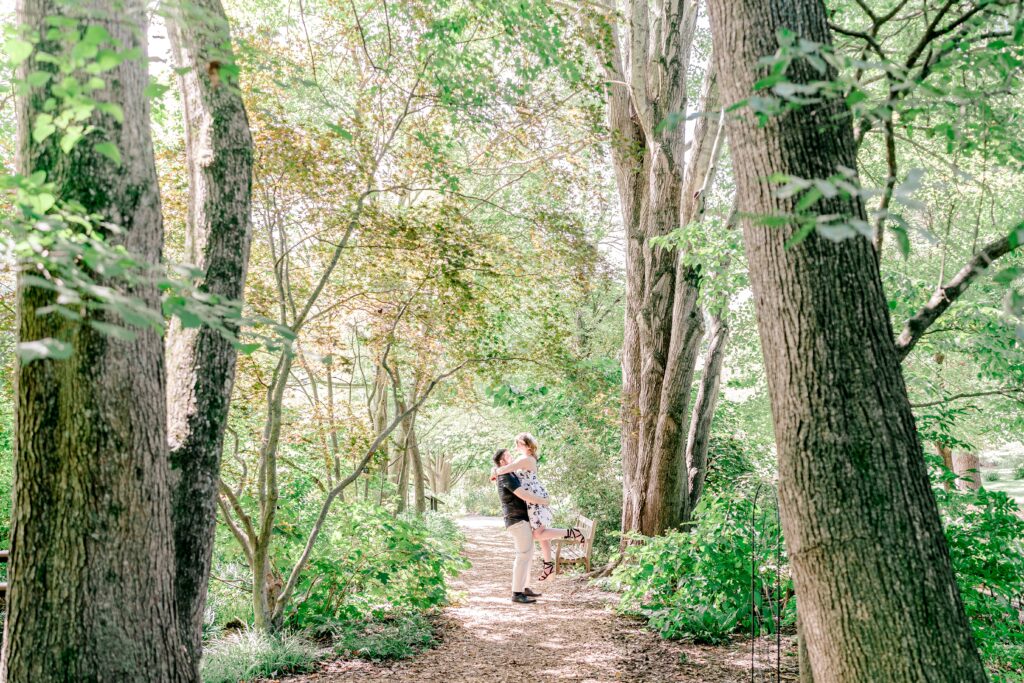A man lifts his partner off the ground surrounded by greenery on a sunny day at the best place to take engagement photos near DC