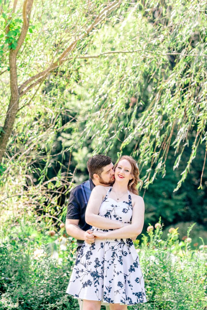 A man kisses his partner's cheek as she smiles at the camera during their Meadowlark Botanical Gardens engagement photos
