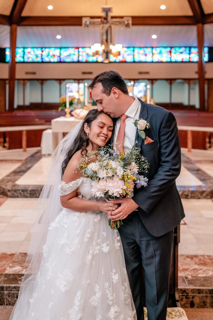 A groom kisses his bride on the head inside the church before their Murray Hill wedding