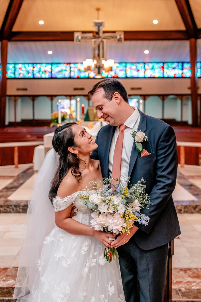 A bride and groom smiling at each other in the church during a St. John the Beloved wedding