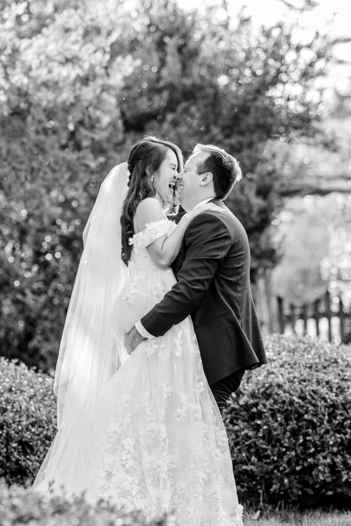 A bride and groom laughing as he lifts her off the ground in the garden during their Loudoun County wedding
