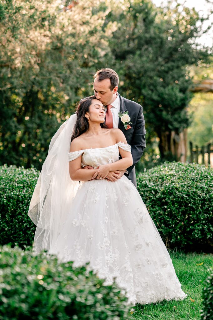 A groom kisses the top of his bride's head during a St. John the Beloved wedding