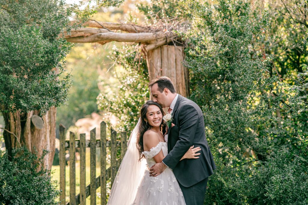 A groom kisses the top of his bride's head in the garden during a Murray Hill wedding