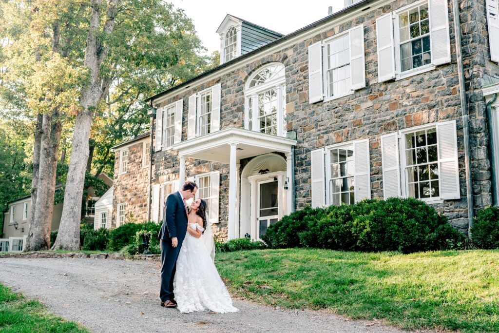 A bride and groom pose in front of the manor house during their Murray Hill wedding