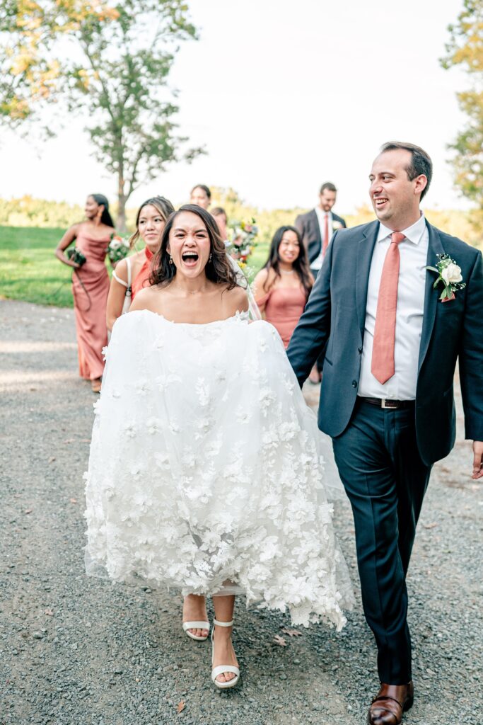 A bride laughing as she walks with her bridal party after a St. John the Beloved wedding