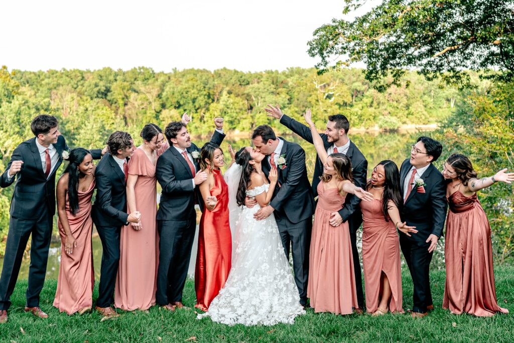 A wedding party cheers as the bride and groom kiss