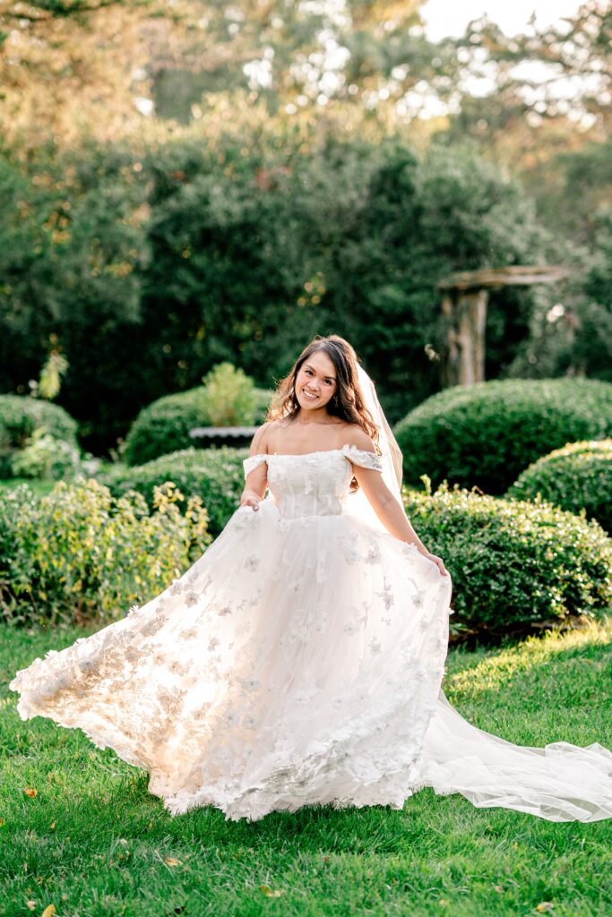 A bride smiles at the camera as she twirls her skirt in the garden