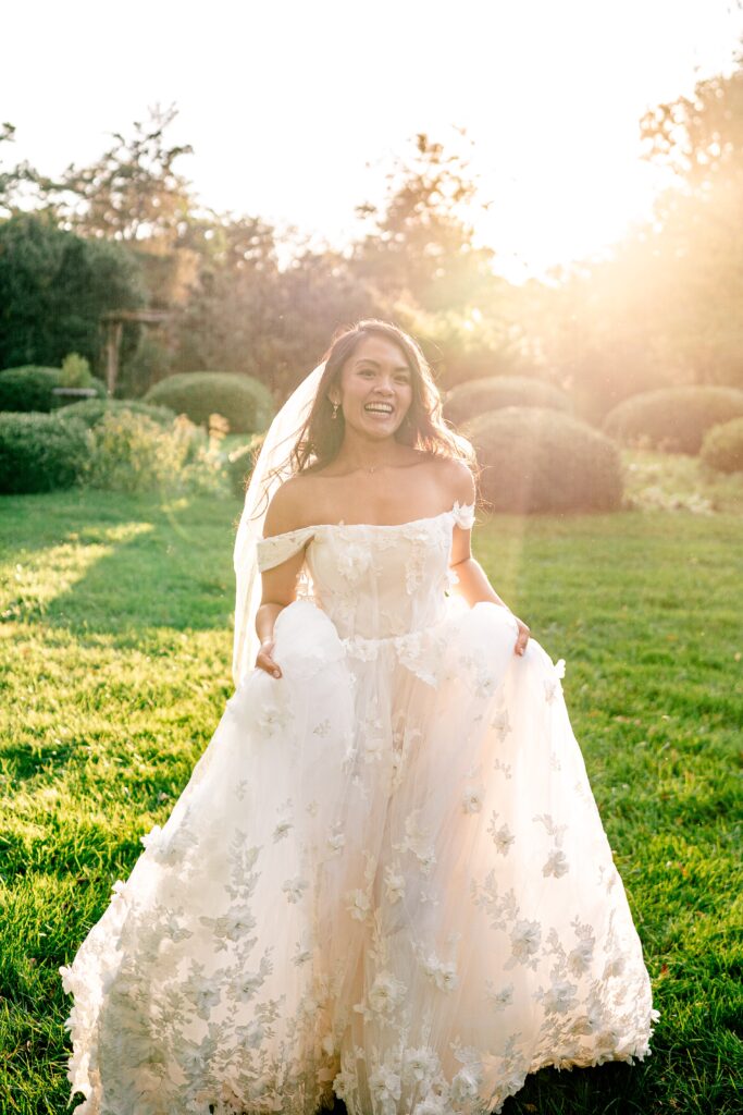 A bride smiles at the camera as she walks with her skirt in her hands