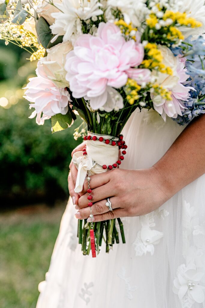 A close up of a bride's hand holding her bouquet with a rosary wrapped around the base for her Murray Hill wedding