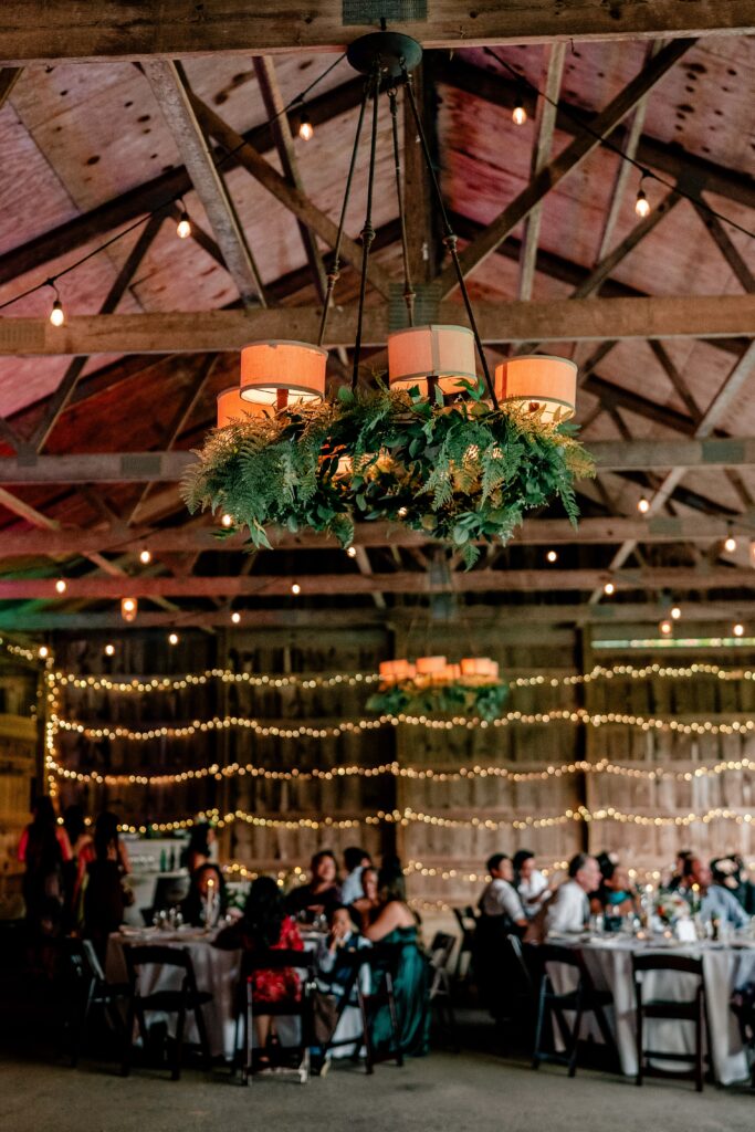 The barn for a Murray Hill wedding with string lights on the wall and greenery on the chandeliers