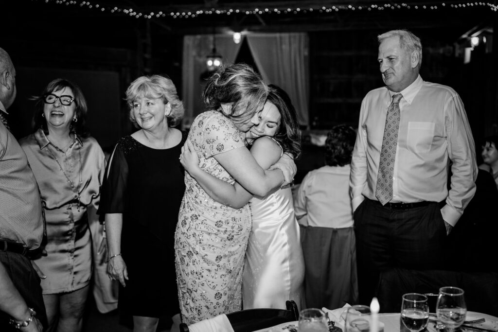A bride and her mother in law share a hug at the reception