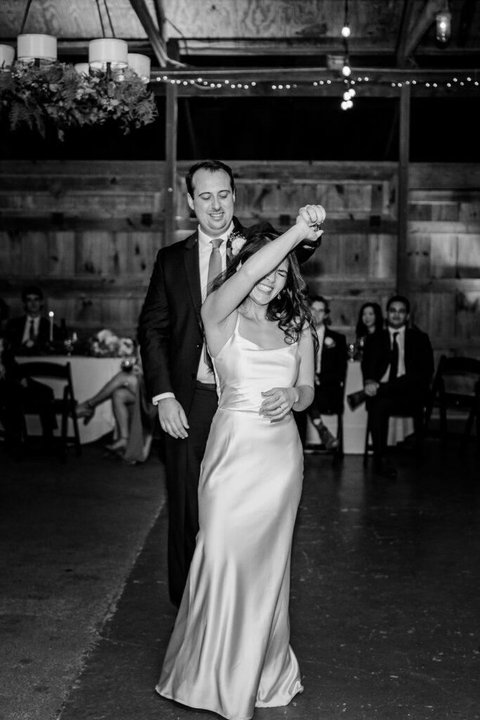 A bride laughs as her groom twirls her during their first dance