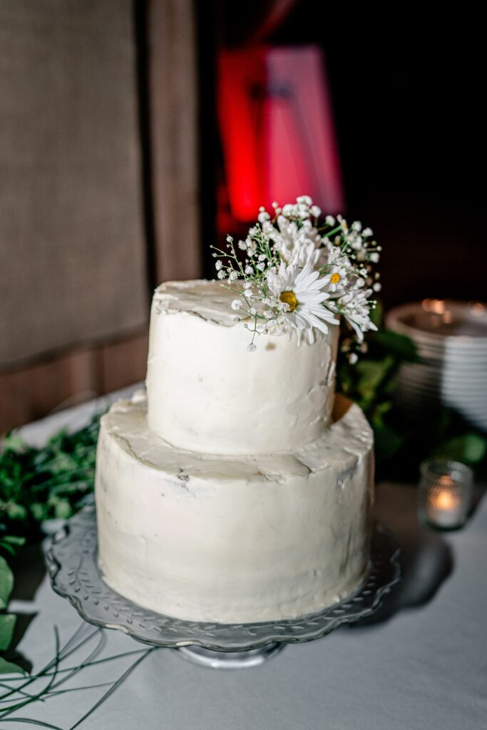 A homemade wedding cake with plain white frosting and daisies on top