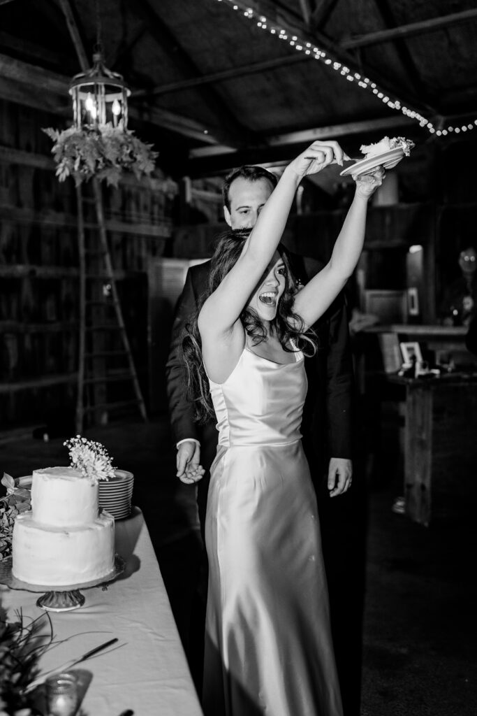 A bride laughing as she lifts a plate of cake in the air during her Murray Hill wedding reception