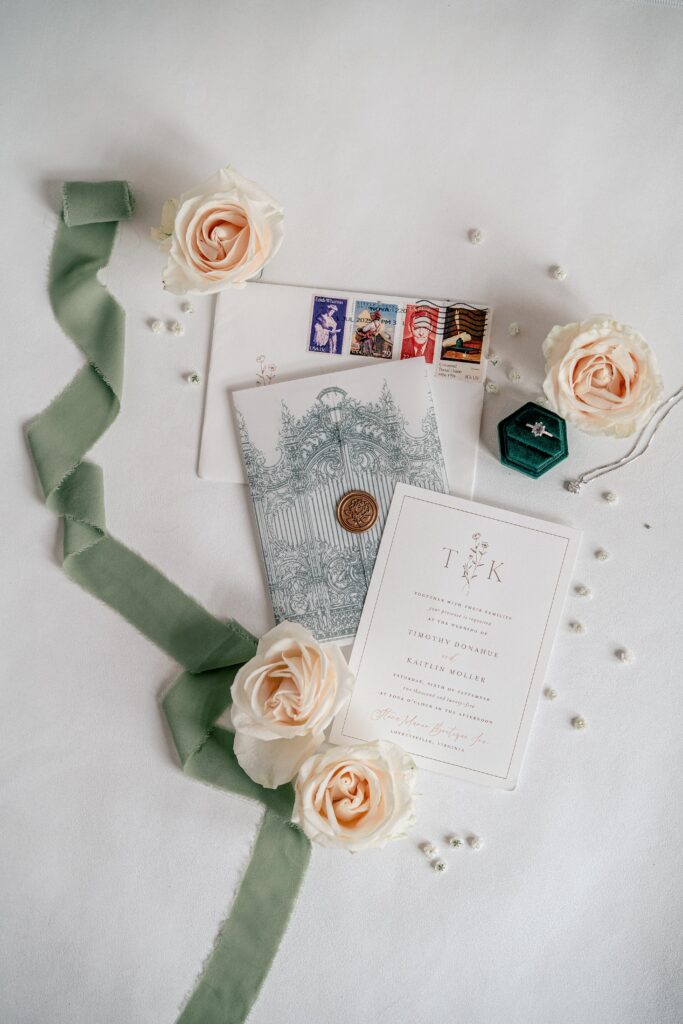 A flat lay of wedding details featuring an invitation suite surrounded by white flowers and a green ribbon