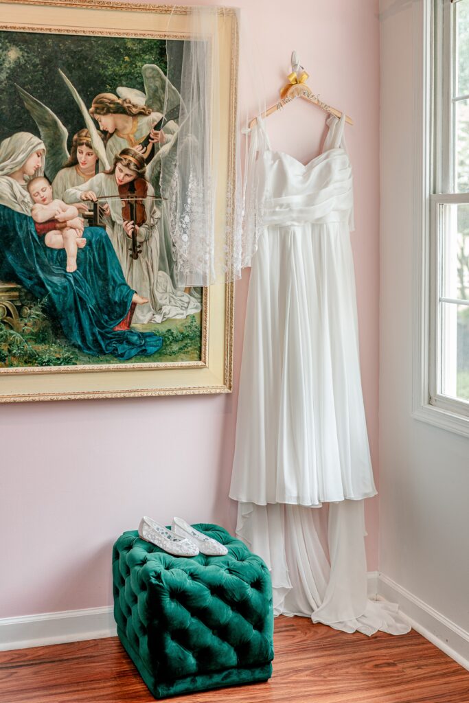 A dress hanging beside a beautiful painting in the bridal suite for a Stone Manor Boutique Inn wedding