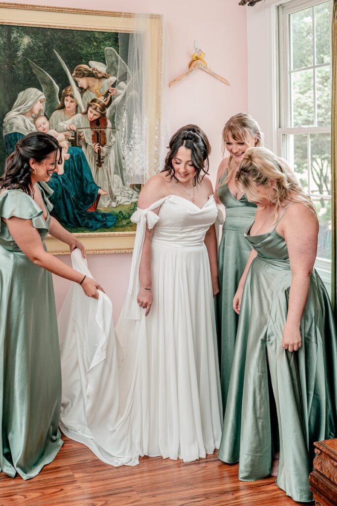 A bride surrounded by bridesmaids as she gets dressed in front of a painting of Mary and the Infant Jesus visited by angels