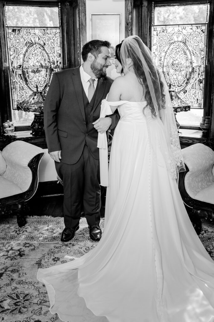 A bride and groom smiling at one another in a sitting room of their venue for a Stone Manor Boutique Inn wedding
