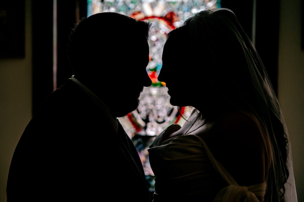 A silhouette of a bride and groom against a stained glass window