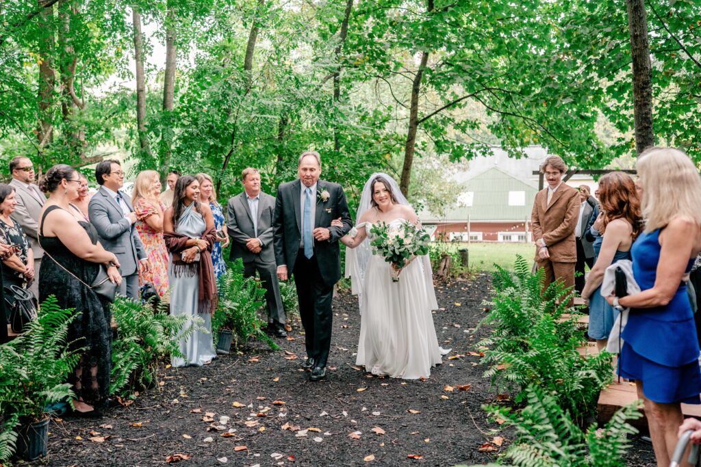 A bride smiling at guests as she walks down the aisle with her father