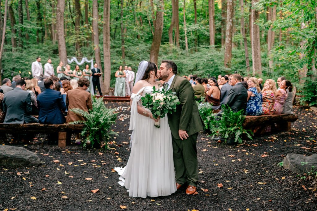 A bride and groom sharing a kiss at the end of the aisle when prompted by their Northern VA wedding photographer