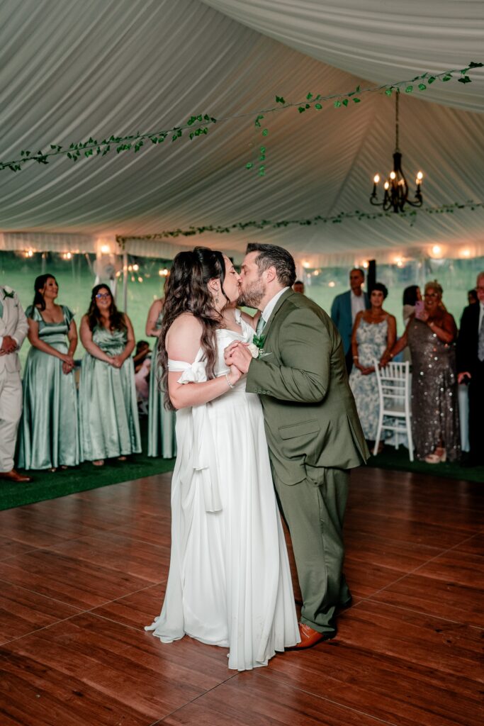 A bride and groom share a kiss on the dance floor as they enter their tented wedding reception