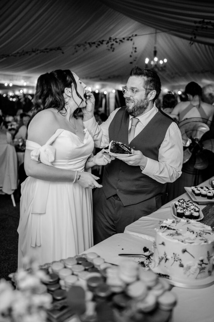 A groom feeds his bride cake during their tented reception