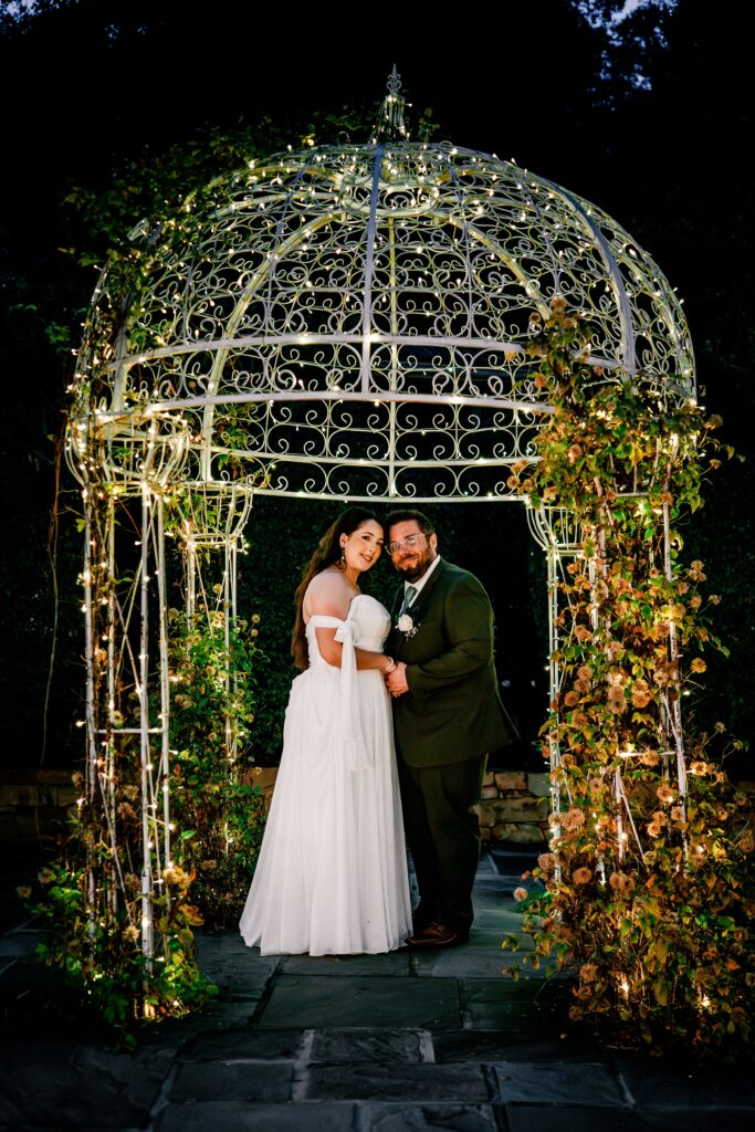 A bride and groom posed under a pergola with string lights for a night portrait during their Loudoun County wedding