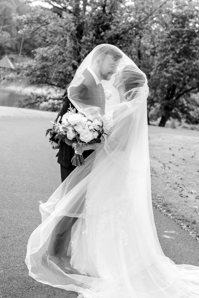A bride and groom looking at one another under her cathedral length veil as it blows in the breeze around them