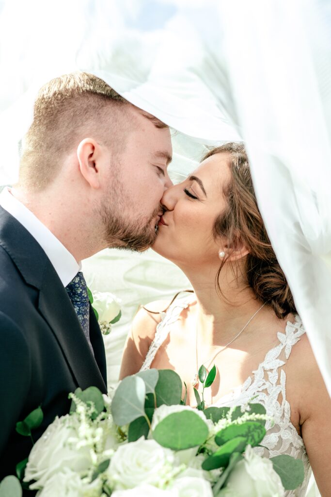 A bride and groom share a kiss under the veil during their Atrium at Meadowlark wedding