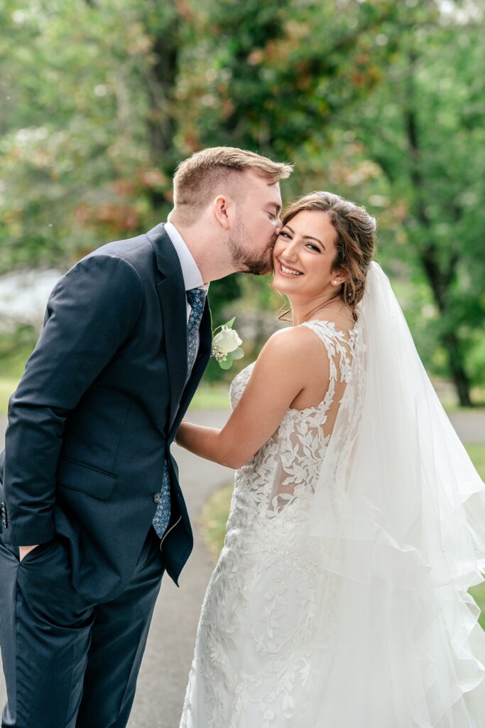 A groom kisses his bride on the cheek at an Atrium at Meadowlark wedding